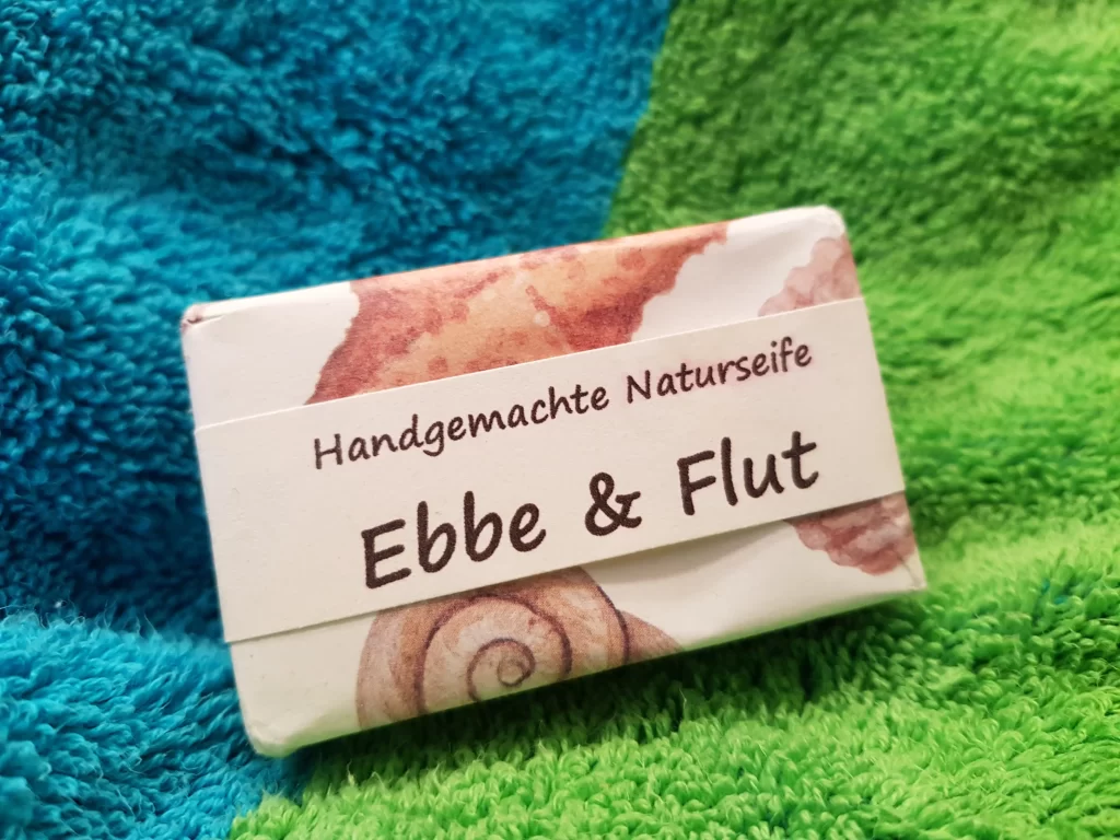 Seifenpäckchen handgemachte Seife "Ebbe und Flut"liegt auf grünblau-farbigen Frotteehandtuch